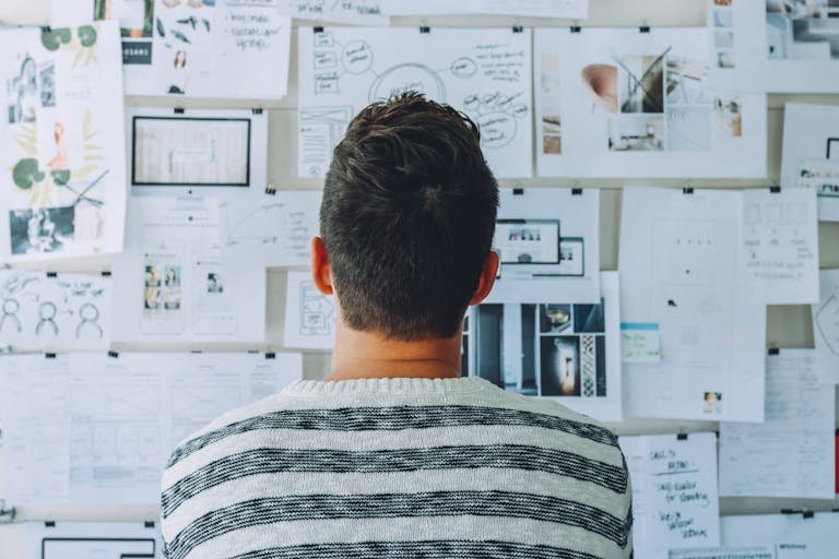 A man stands in front of a wall filled with creative ideas and plans. Ideal for innovation themes.
