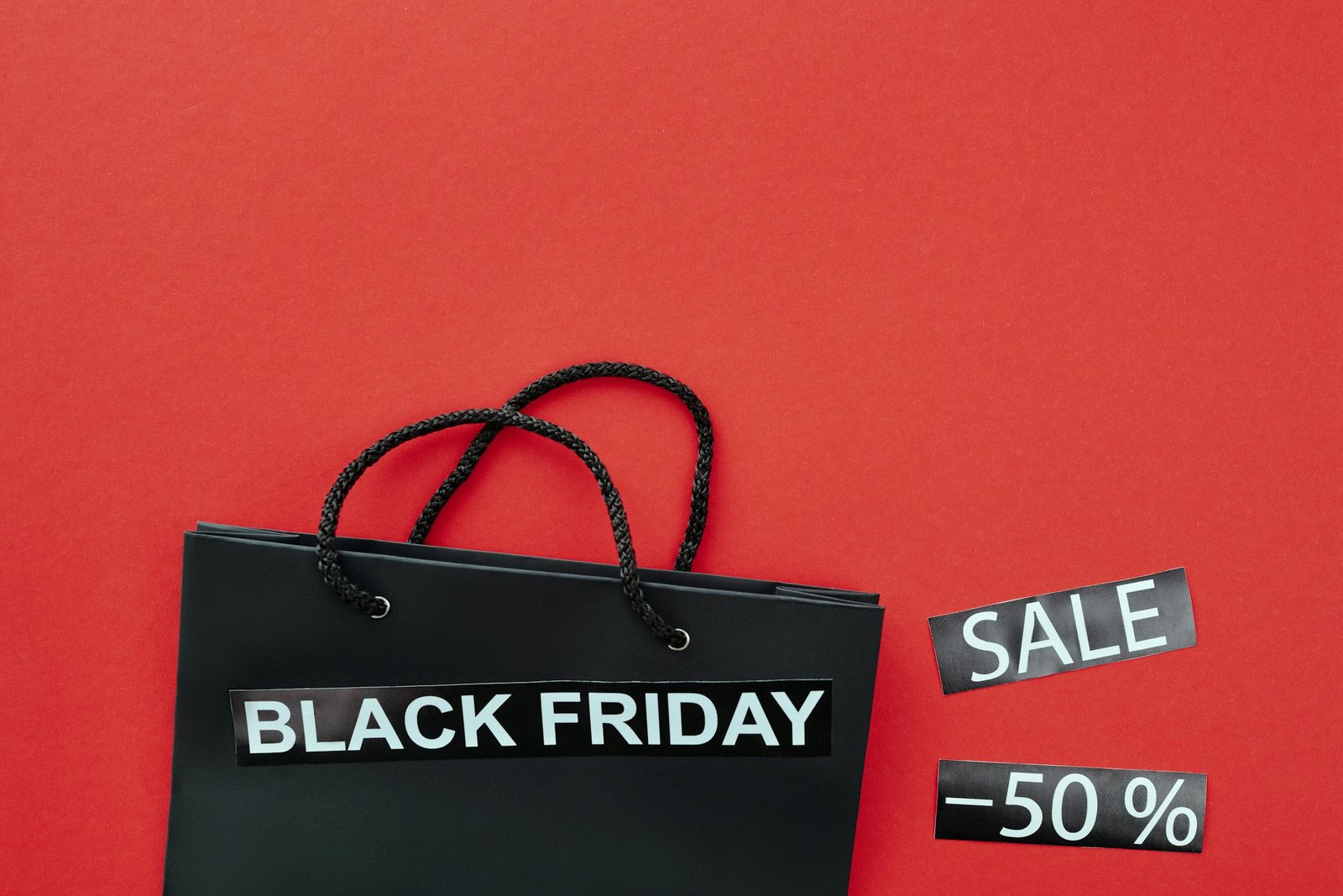 Black Friday shopping bag with sale tags on a vibrant red background.